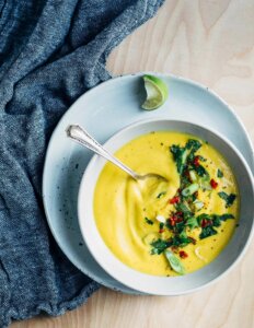 A bowl of vibrant yellow cauliflower soup topped with herbs and green onions.