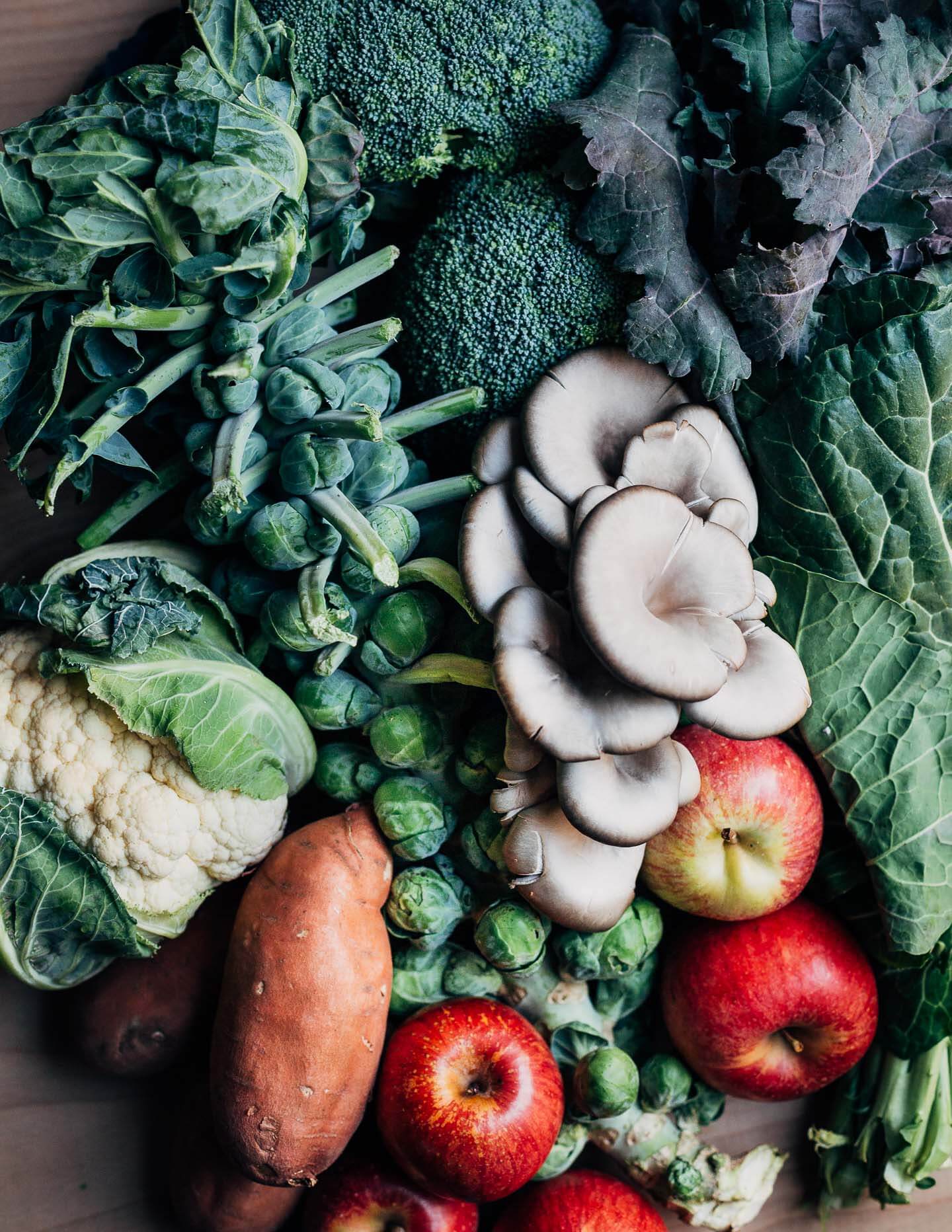 A table filled with fresh produce, including cauliflower, apples, greens, and Brussels sprouts.