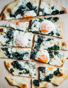 An egg and greens pizza, sliced.