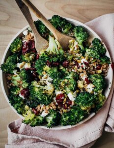 A bowl of roasted broccoli salad with wooden serving utensils.