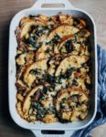 A baking dish with savory bread pudding and a dish cloth on the side.