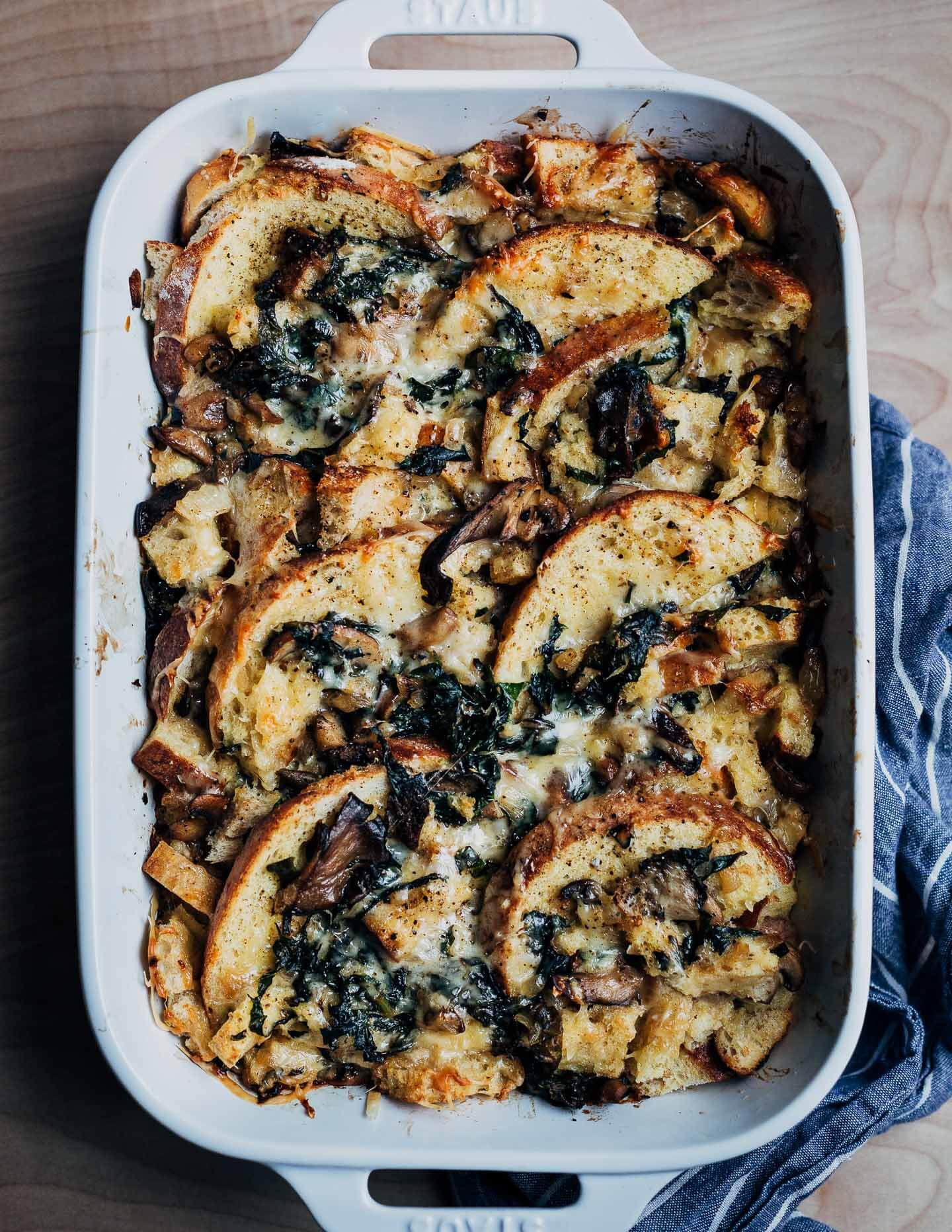 A baking dish with savory bread pudding and a dish cloth on the side. 