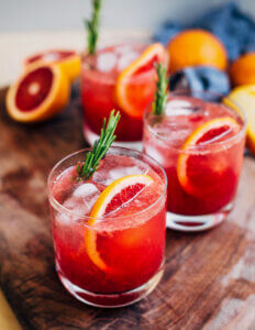 Glasses of bright pink blood orange spritzers on a dark cutting board.