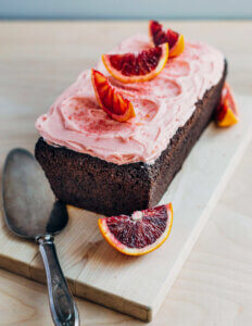 A chocolate cake with pink frosting and orange slices on a small wooden cutting board.