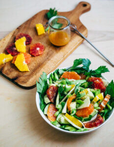 A bowl of salad next to a cutting board with ingredients.