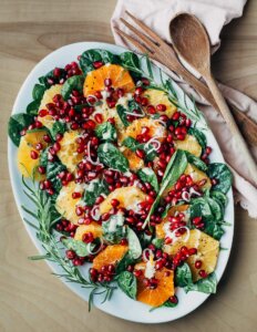 An orange and pomegranate salad on a big platter with serving utensils alongside.