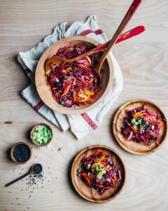 A bowl of colorful red cabbage salad with two wooden plates alongside.