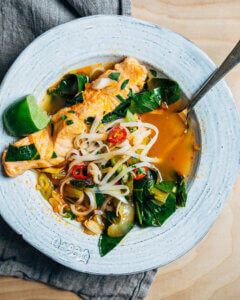 A bowl of curry soup with rice noodles, bok choy, and salmon.