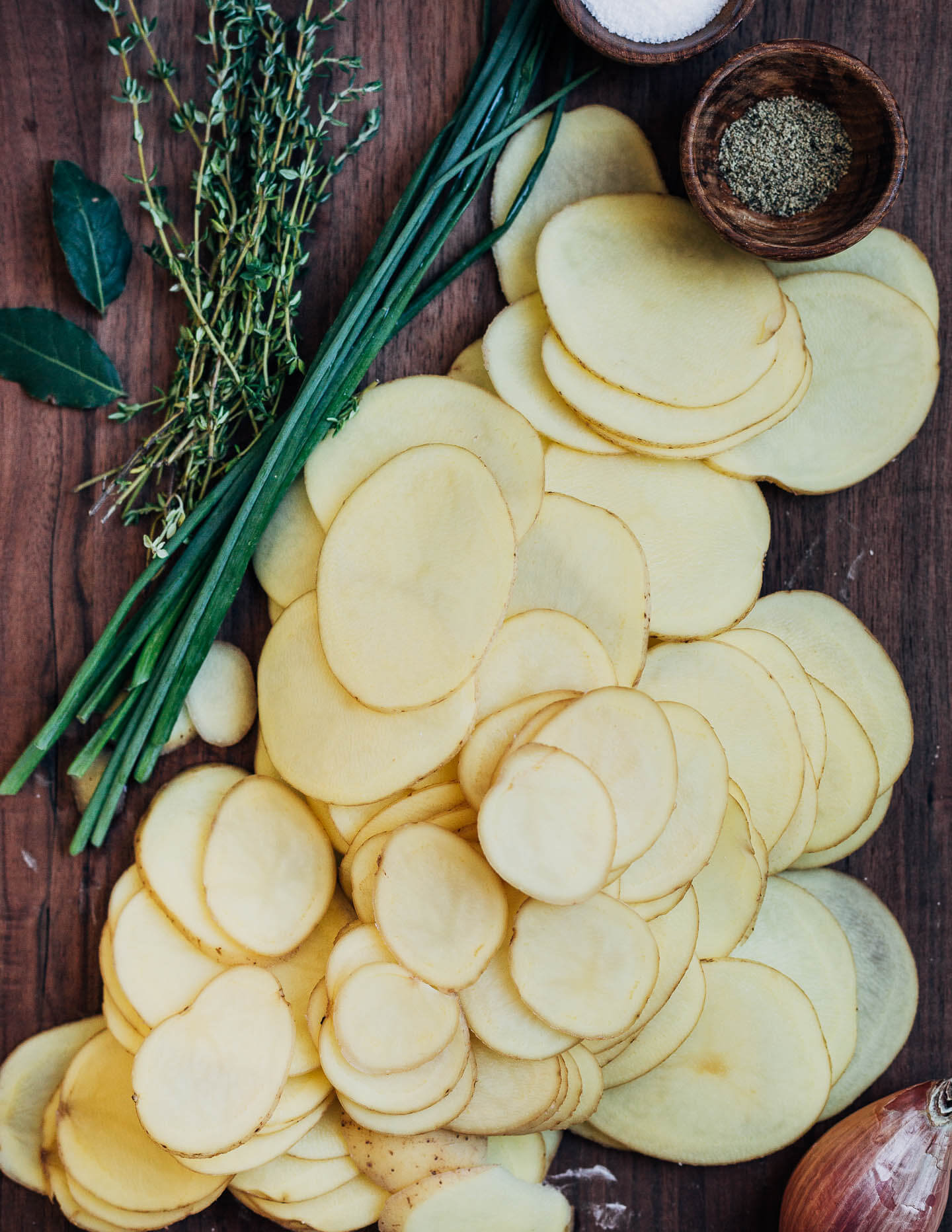 A cutting board with sliced potatoes and herbs. 