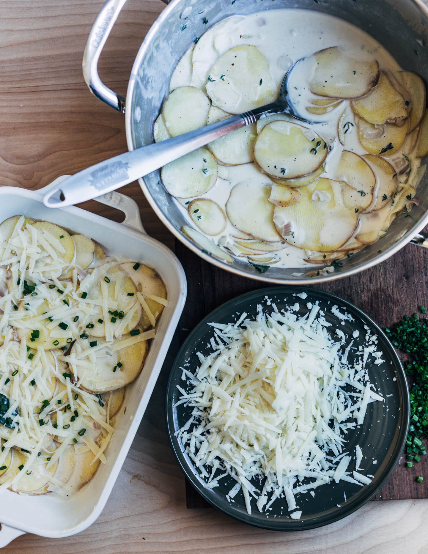 A work table with a pot of potatoes and cream, a baking dish, and grated cheese. 