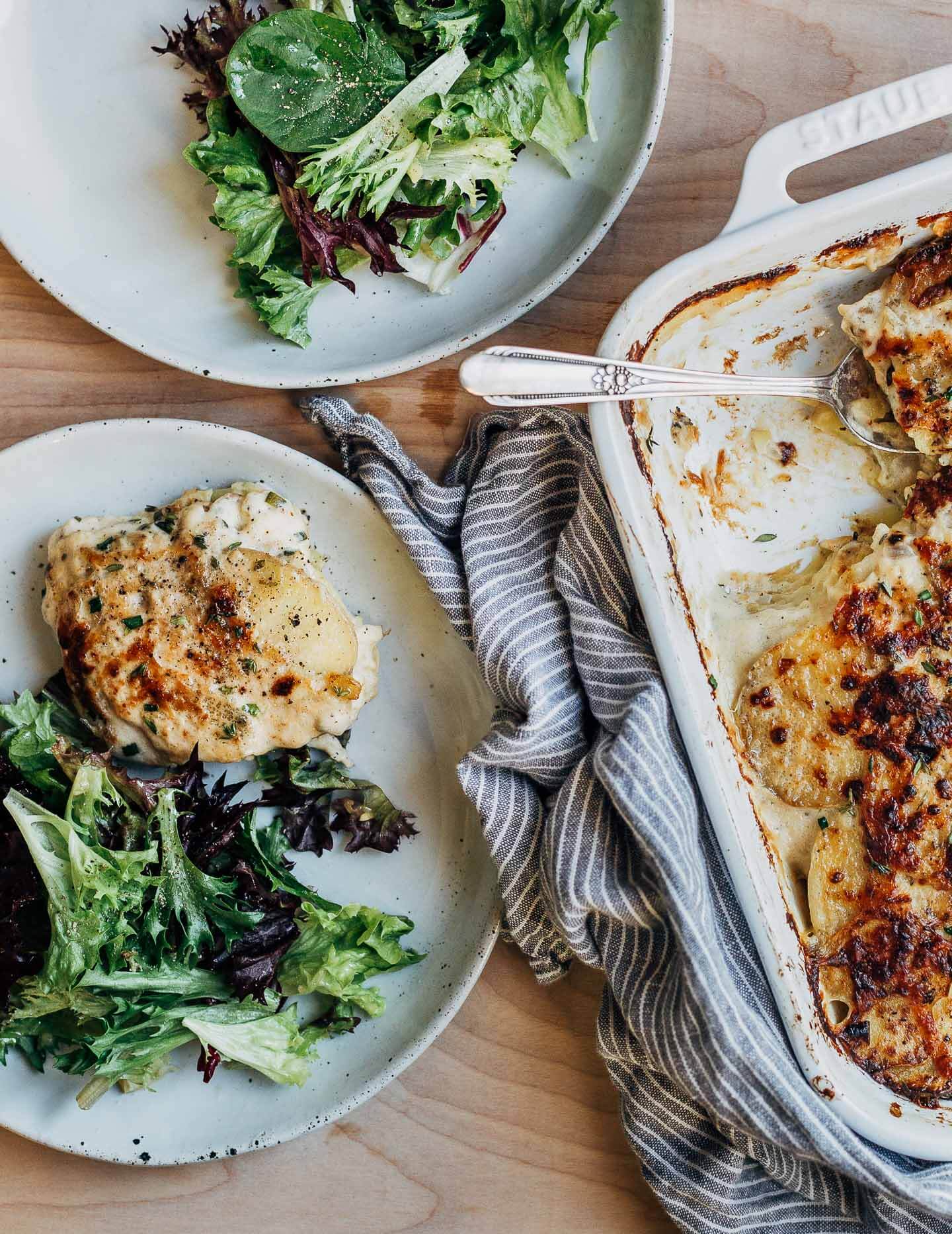 Serving slices of scalloped potatoes on plates with salad. 