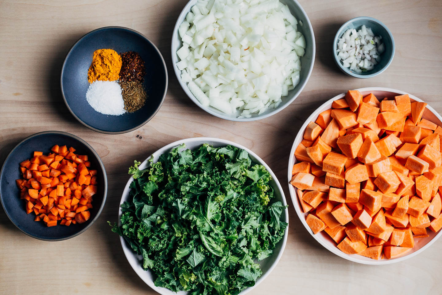 Bowls with ingredients for sweet potato stew laid out on a table. 