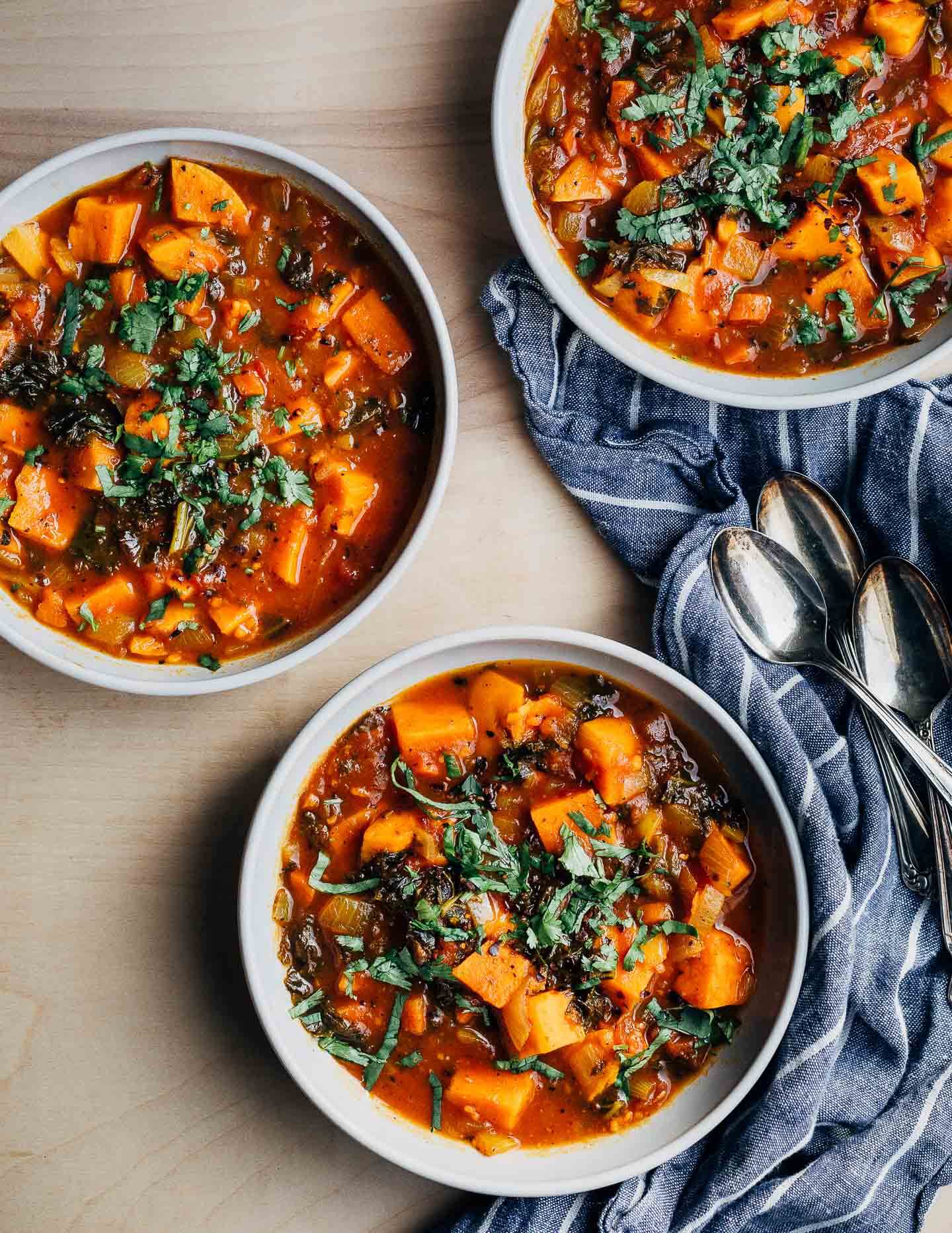 Three bowls of sweet potato stew with a blue cloth napkin and spoons. 