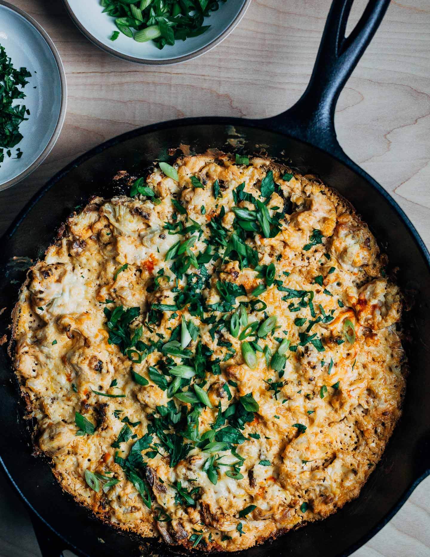 A skillet Buffalo cauliflower dip topped with green onions and parsley. 