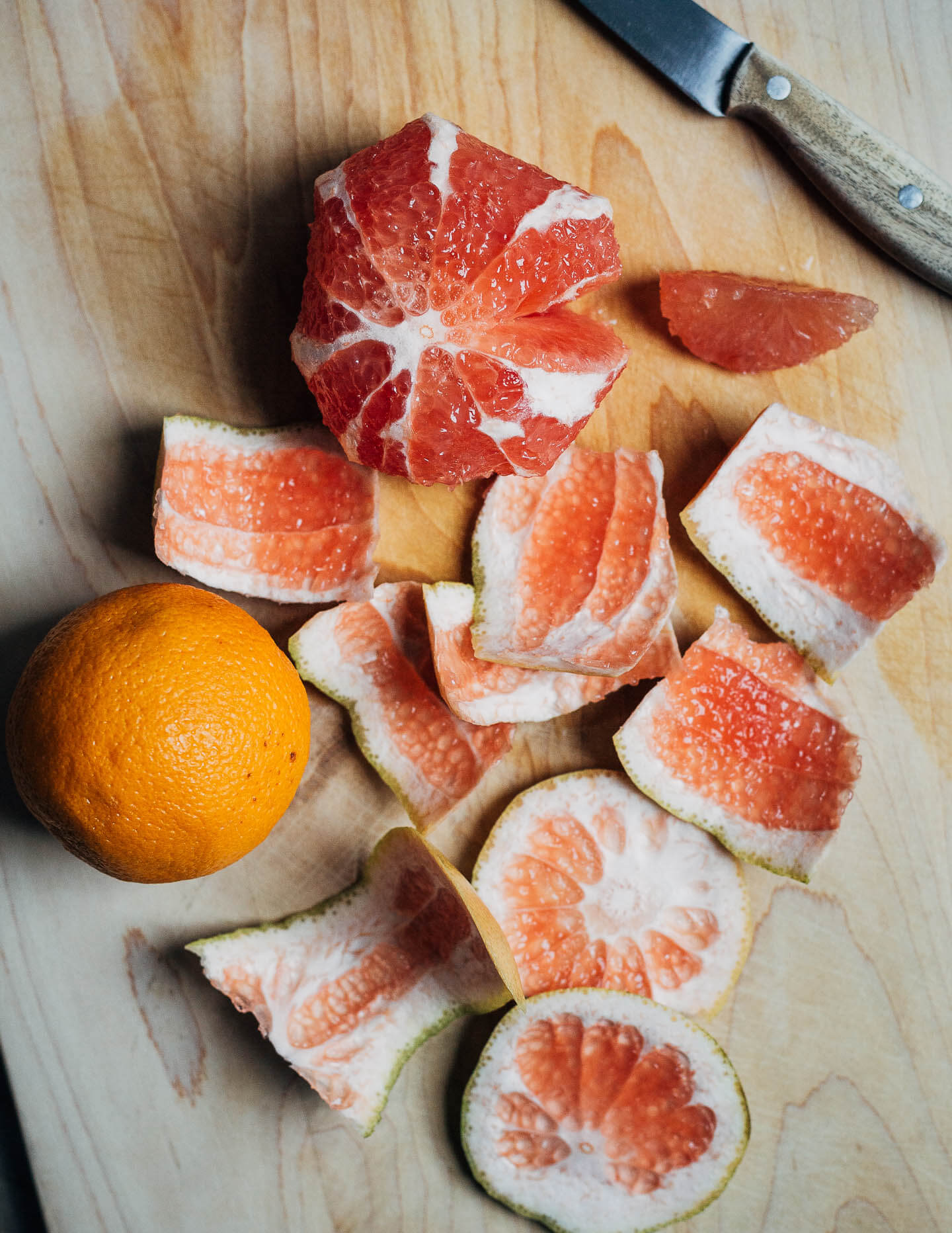 A cutting board with segmented grapefruits and an orange. 