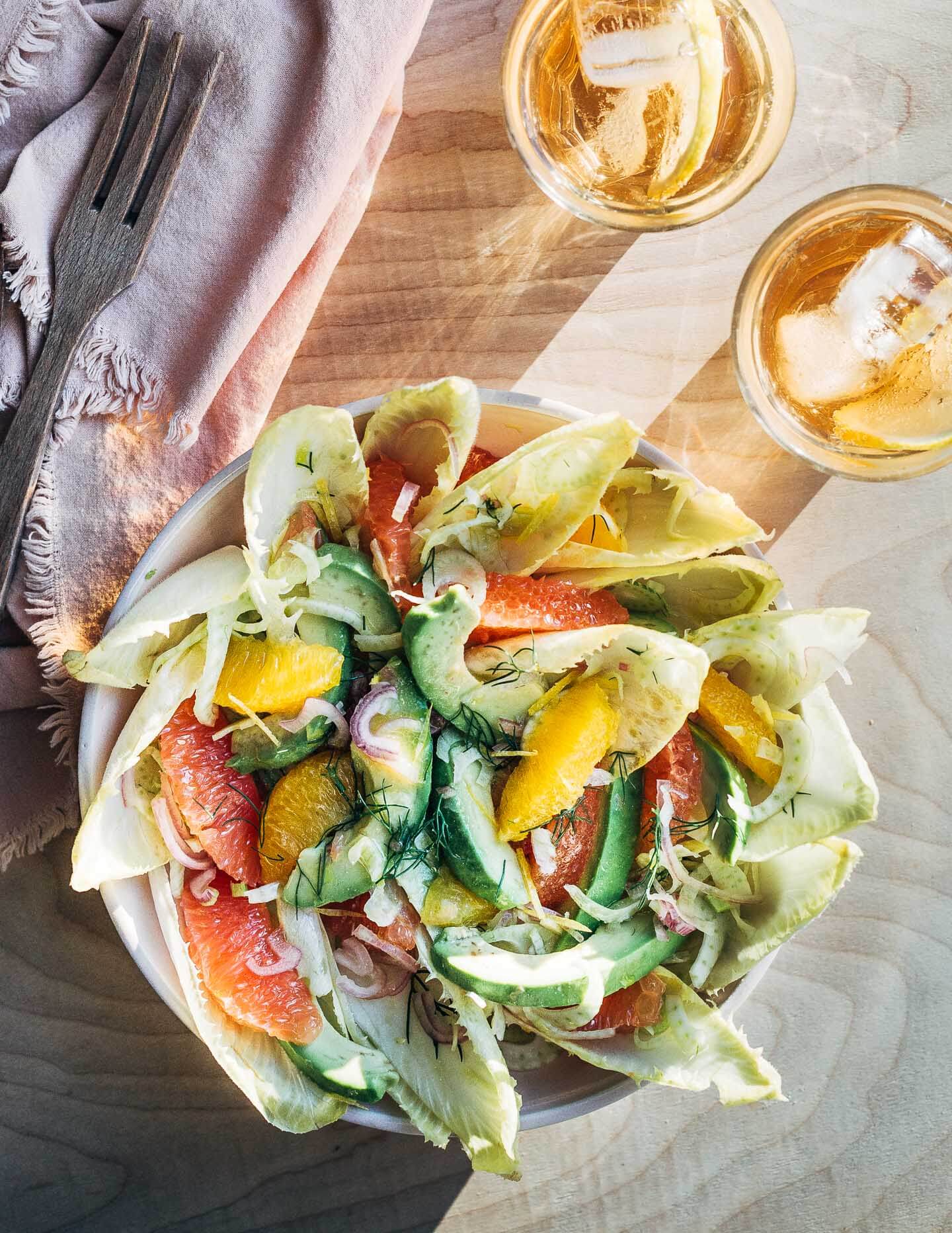 A bowl of salad, with drinks and cutlery in bright, raking sunlight. 