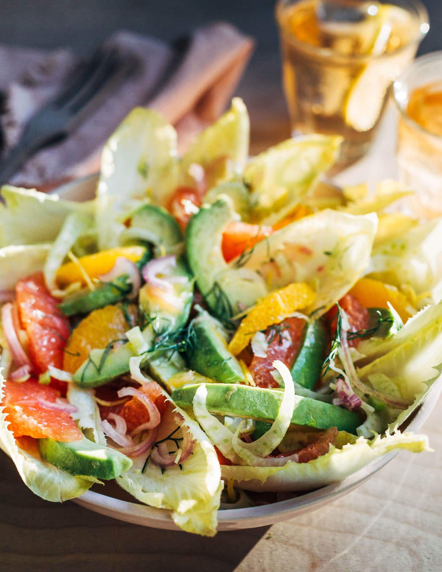 A bowl of salad, with drinks and cutlery in bright sunlight. 