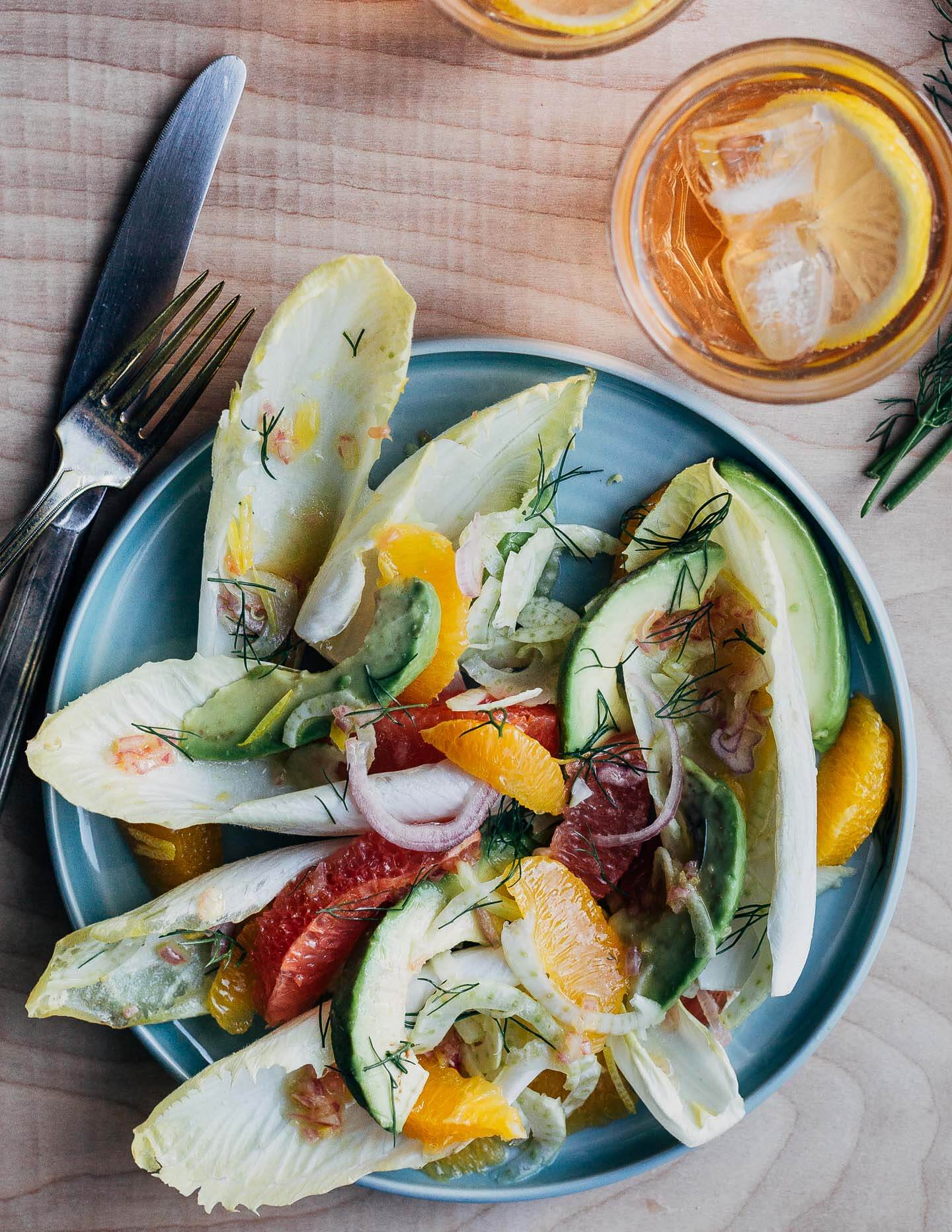 A plate with endive salad, with a pink drink and cutlerey alongside. 