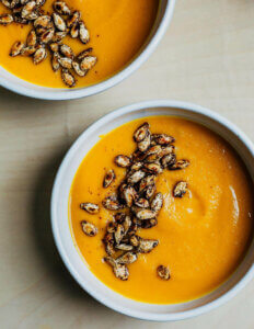 Tow bowls of squash soup topped with squash seeds