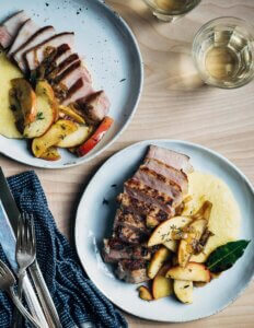 Two plates with sliced pork, polenta, and apples.
