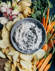 A bowl of onion dip surrounded by chips and veggies.
