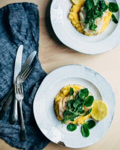 Two shallow bowls with pureed rutabaga, poached cod, and watercress.