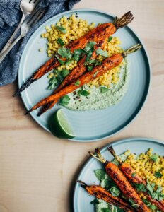 Two plates with roasted carrots, with cousocus and green tahini.