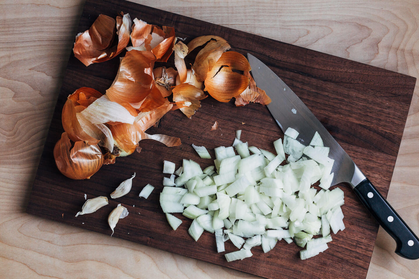 A cutting board with onion skins and diced onions.
