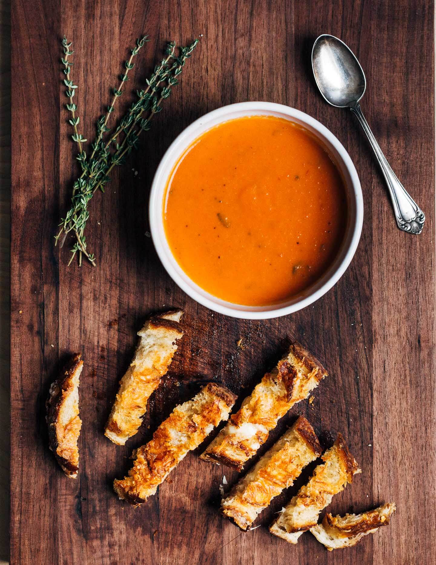 A bowl of soup and sliced grilled cheese on a cutting board.