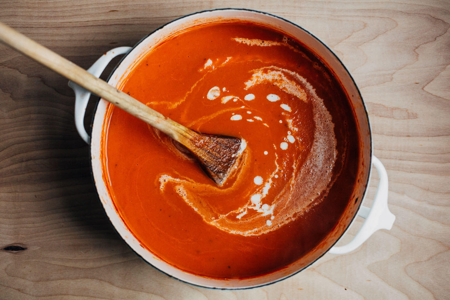 A pot of tomato soup with a swirl of cream.