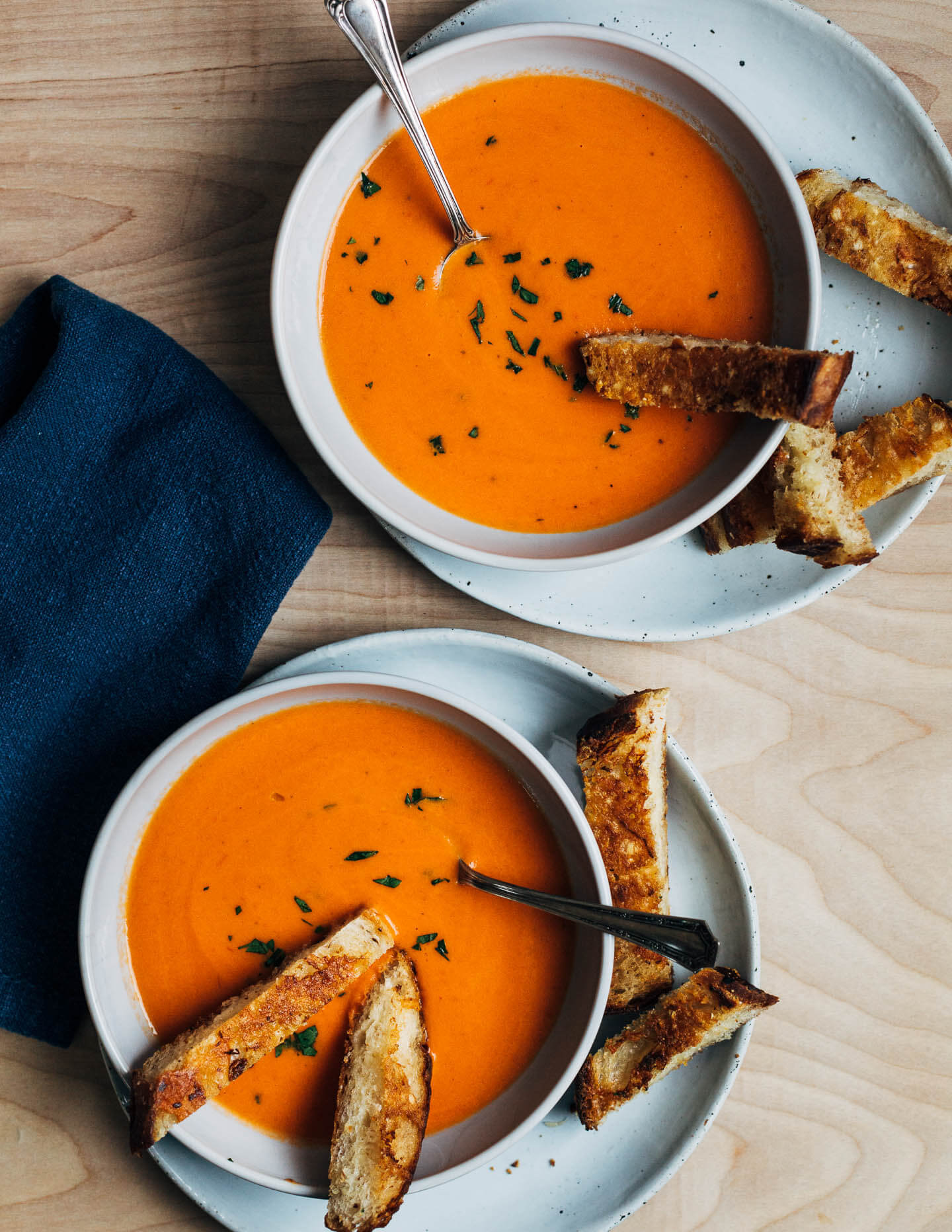 Two bowls of tomato soup with grilled cheese strips dipped in the soup. 