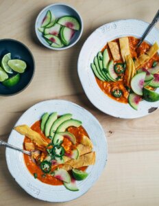 Two bowl of tortilla soup with sliced radishes and avocados.