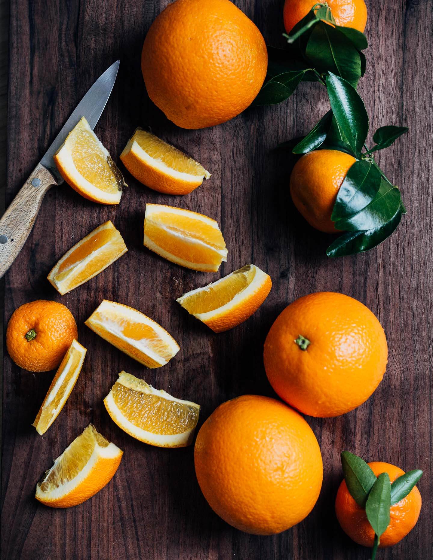 A cutting board with whole and sliced oranges.