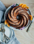 A swirled bundt cake garnished with flowers. There are plates, forks, and a knife for serving alongside.