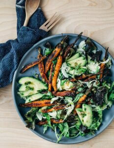 A gray bowl with carrots, avocado, and greens.