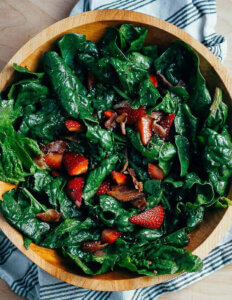 A wooden bowl with spinach, strawberries, and bacon crumbles.