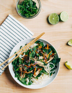 A bowl of rice noodle salad with greens and other vegetables on a set table.