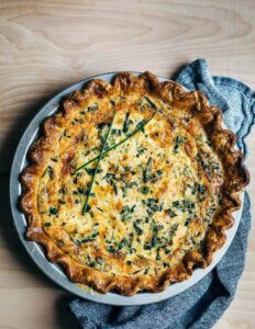 A whole quiche garnished with chives with a napkin alongside.