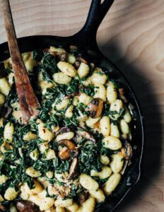 A skillet with gnocchi, mushrooms, and greens.