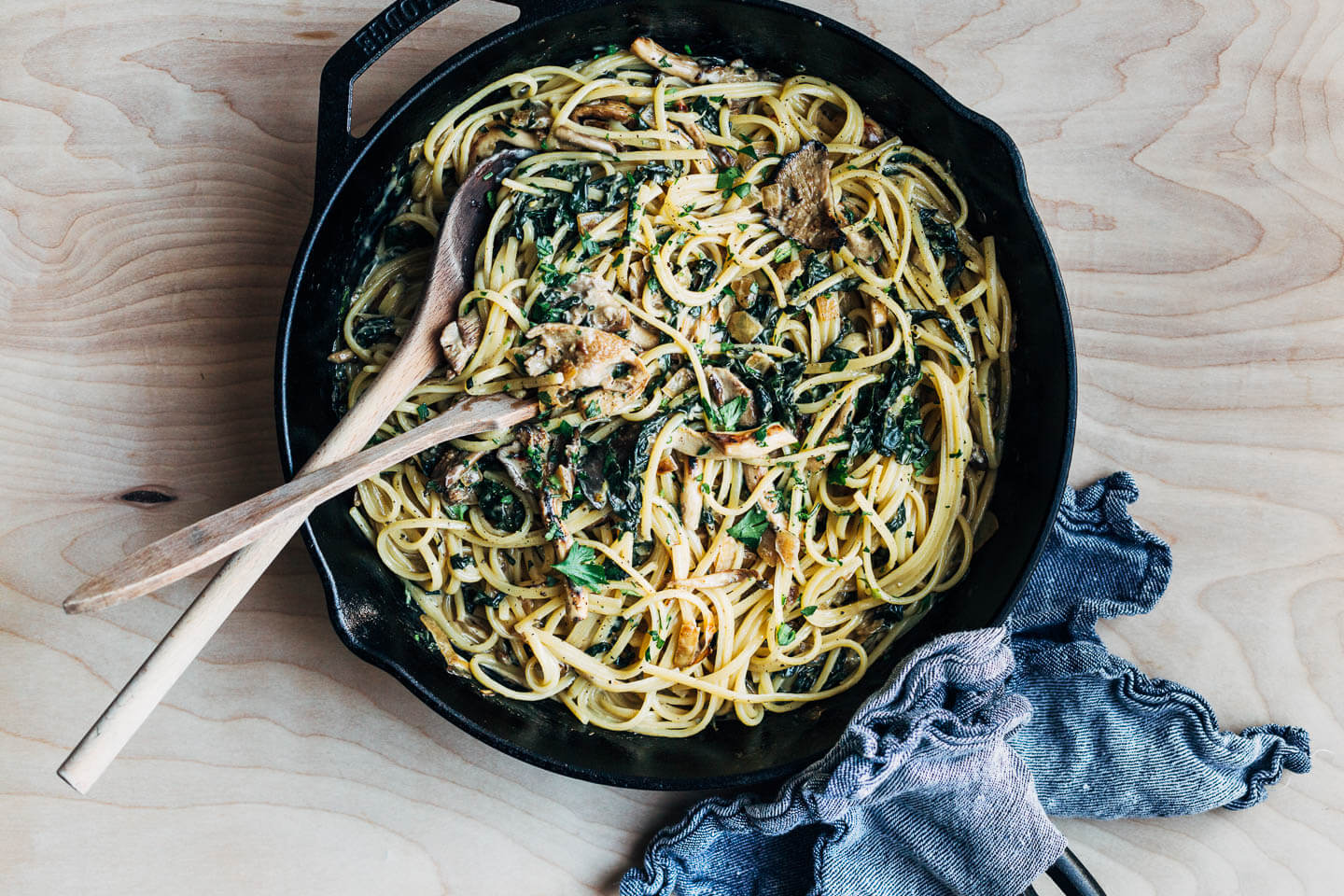 A skillet with linguine, greens, and mushrooms all tossed together. 