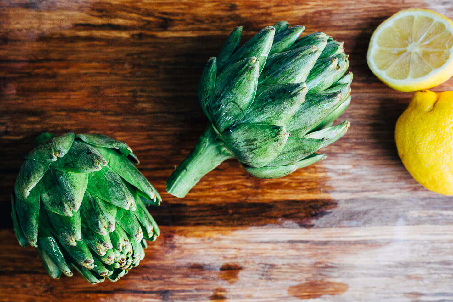 Two whole artichokes on a cutting board. 