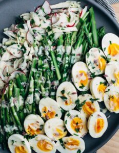 A platter with eggs, asparagus, and radishes.