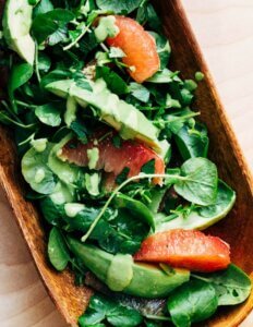 A wooden platter with watercress, grapefruit, and sliced avocado.