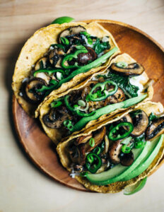 A plate with three mushroom tacos with kale and sliced peppers.