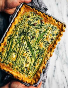 Looking down on a sheet pan quiche with flowers herbs and alliums laid in a decorative arrangement on top.