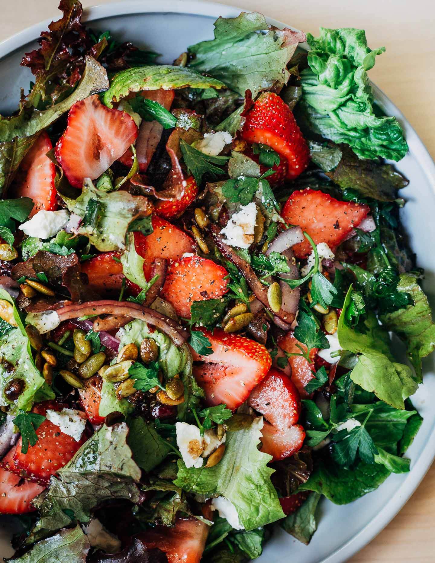 A shallow bowl filled with lettuces, strawberries, and salad other toppings. 