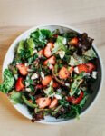 A shallow bowl filled with lettuces, strawberries, and salad other toppings.