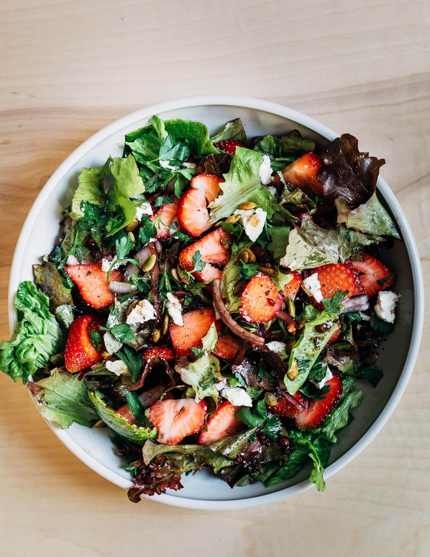 A shallow bowl filled with lettuces, strawberries, and salad other toppings. 