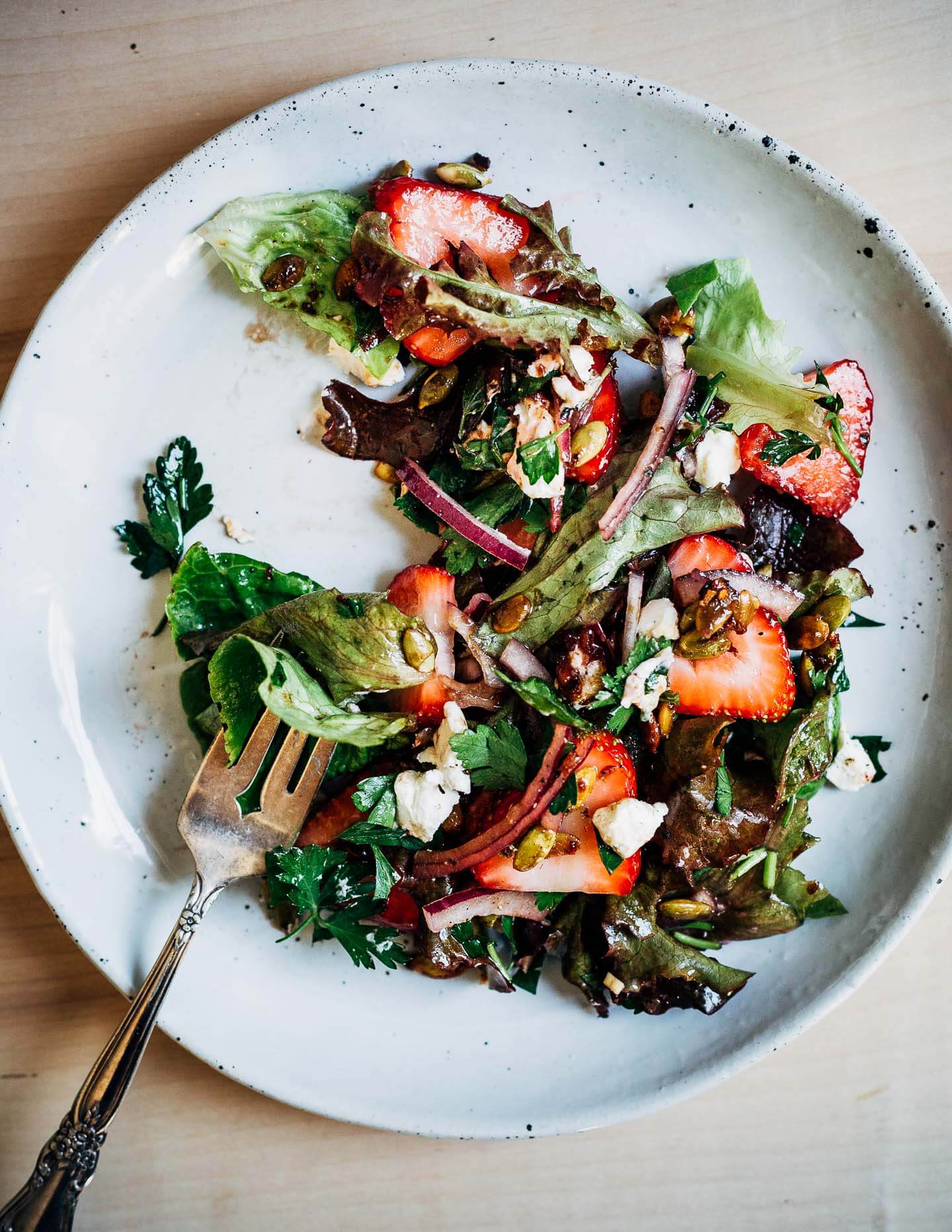 Strawberry salad on a small plate, a fork sits with a bite at the ready. 