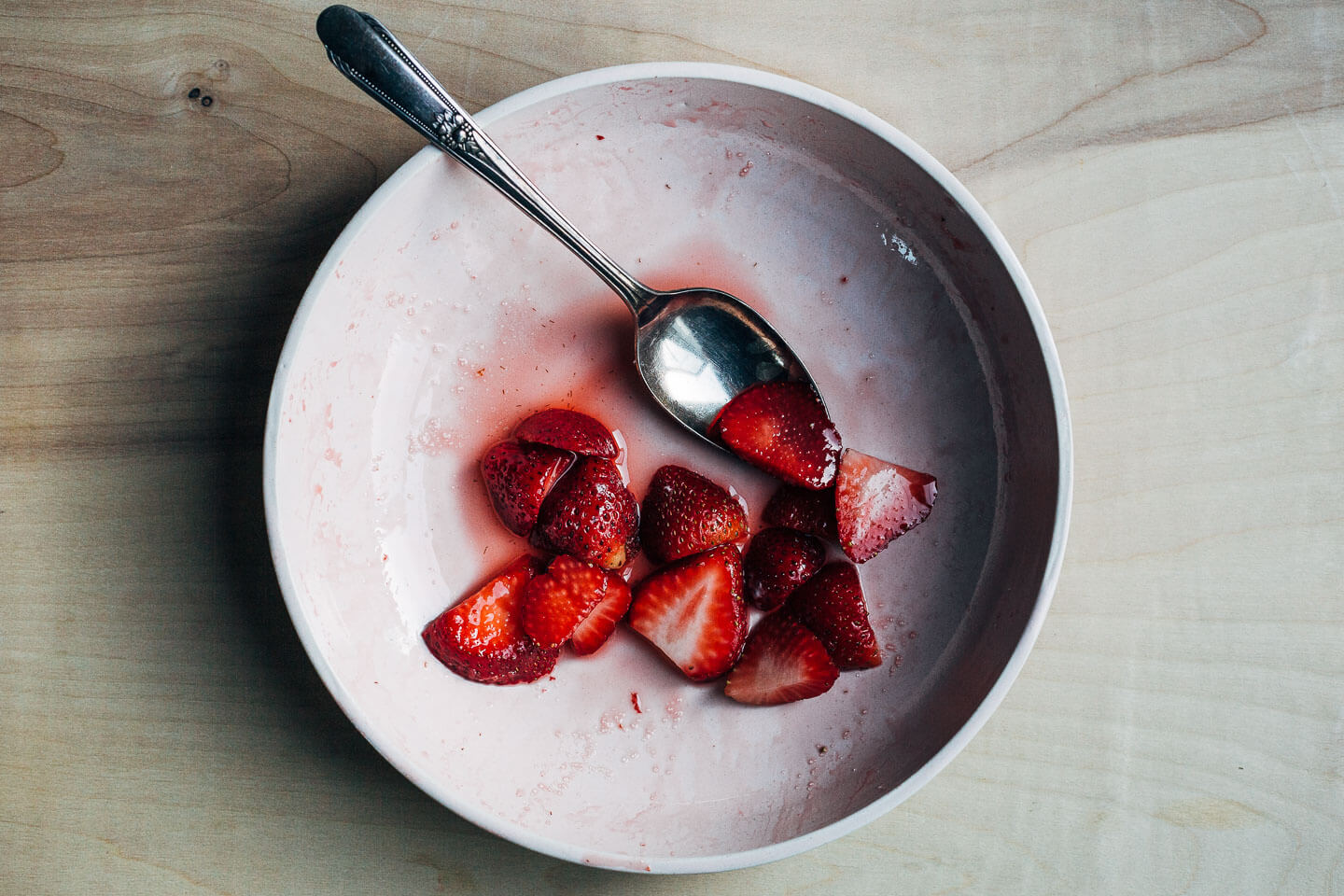 A bowl with just a few sliced strawberries and some of their juice. 